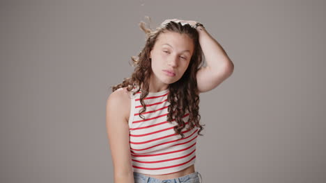 young brunette looks into camera, fixes hair and smiles, studio shot