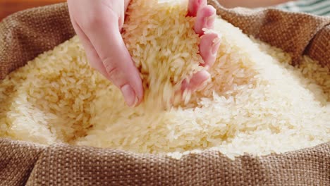 a hand scooping and pouring rice grains from a burlap sack