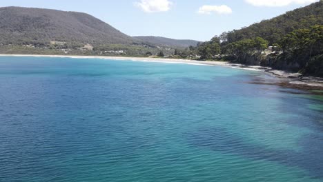 drone aerial slow pan over tropical blue water with mountain on sunny summer day