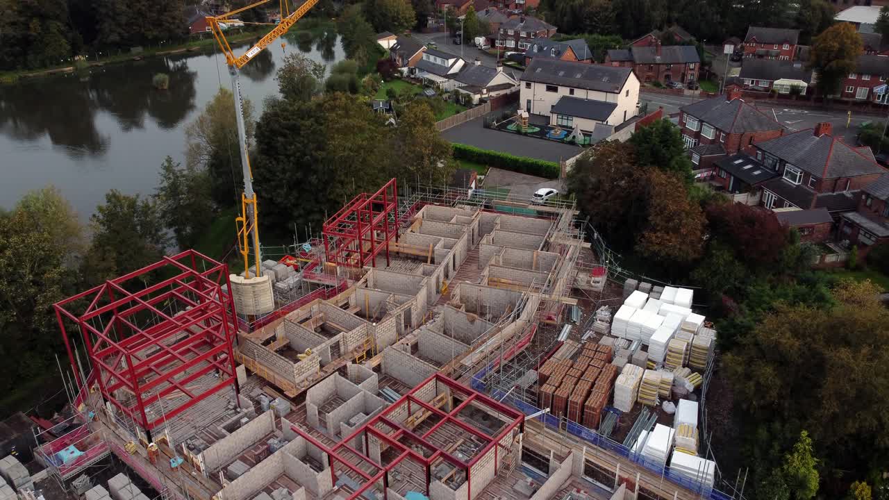 Aerial view looking down over crane care home development site in rural British village next to fishing lake