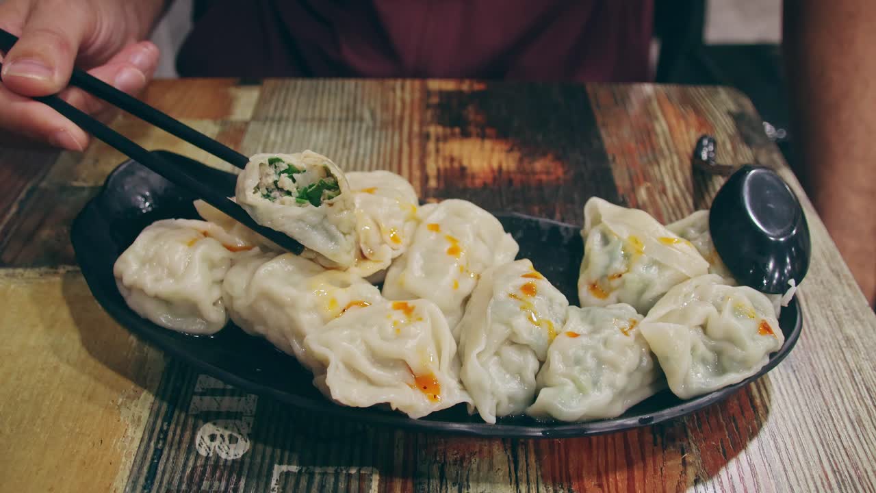 Menikmati sepiring momo kukus tradisional atau pangsit menggunakan sumpit yang disajikan di meja kayu pedesaan, menampilkan pengalaman jujur menikmati hidangan Nepal lokal yang autentik.