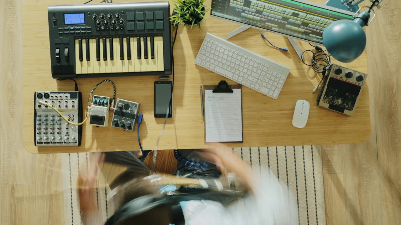 Top view time lapse of young man creating music playing keyboard and guitar at home