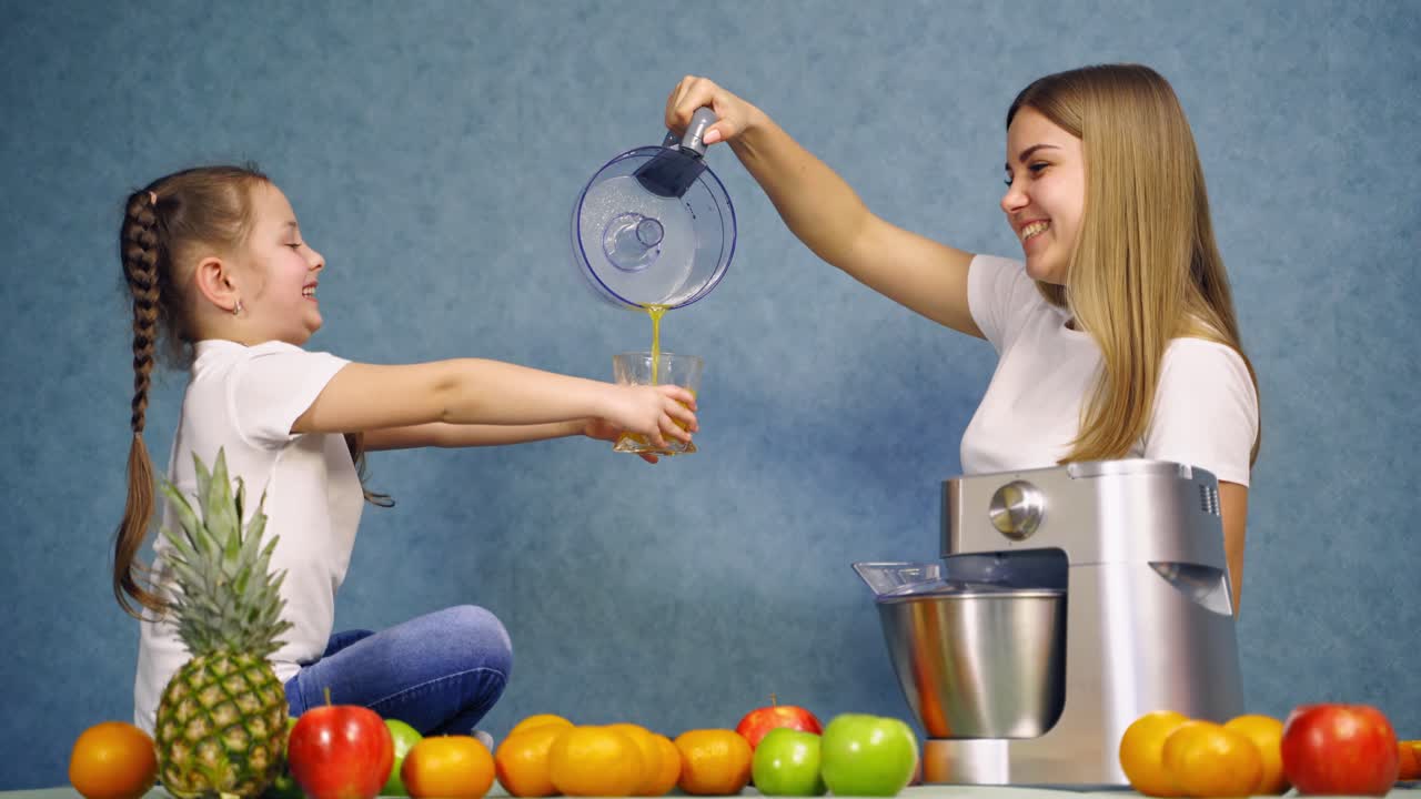 Happy family drinking juice. Smiling girl sitting on the table with fruits and juice