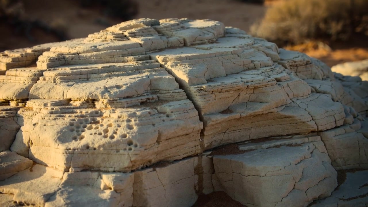 Approaching camera showing pale layered rock in desert, revealing fine detail, fissure and pits
