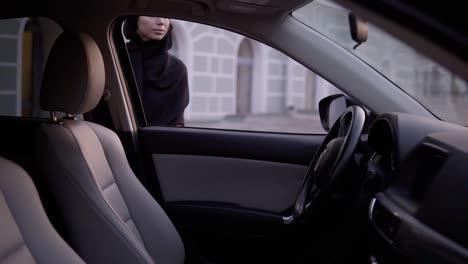 Young-Beautiful-Muslim-Girl-In-Black-Hijab-Open-The-Door-And-Sitting-In-Car,-Watching-At-Mirror,-Fixing-It