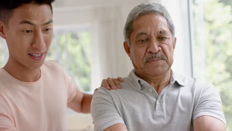 diverse male physiotherapist advising and determined senior man using dumbbells, in slow motion