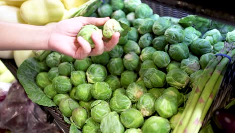 a hand carefully picks brussels sprouts from a vibrant display in a well-lit supermarket setting