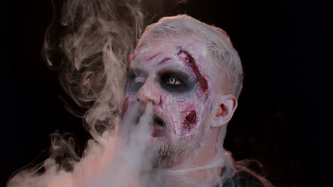 Zombie-man-with-makeup-with-wounds-scars-and-white-contact-lenses-blows-smoke-from-nose-and-mouth