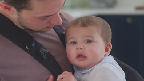 close up of transgender father with baby son in sling at home in kitchen