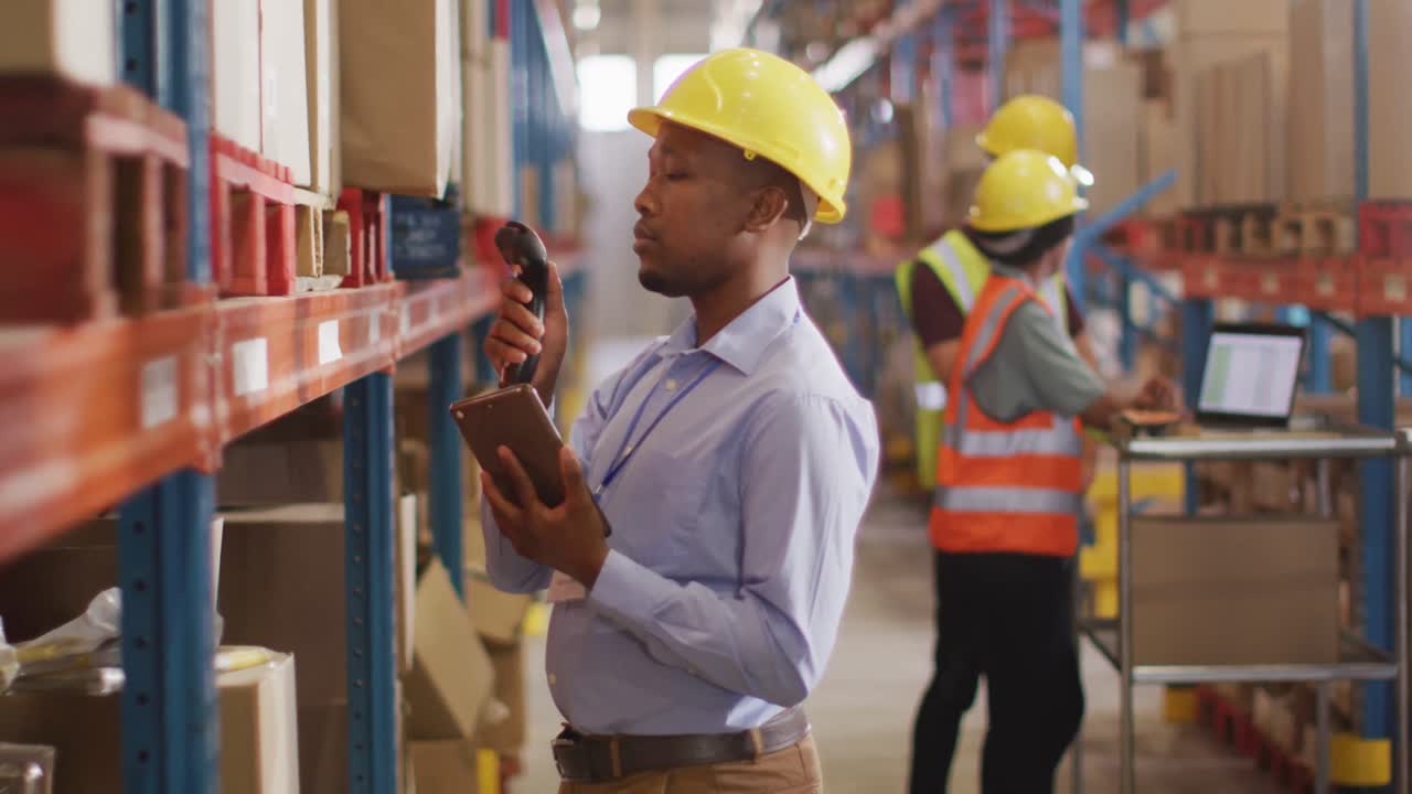 trabajador masculino afroamericano con casco usando un teléfono inteligente en un almacén