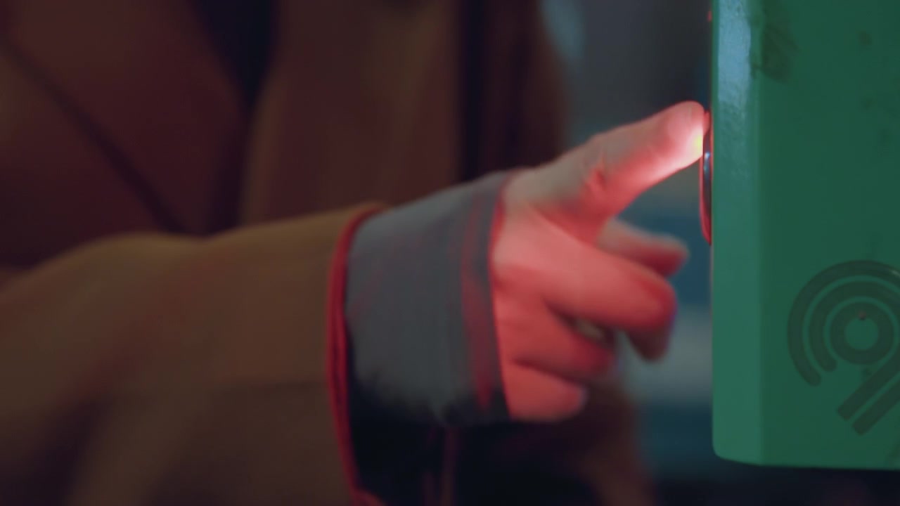 Tocco validatore contactless, donna caucasica che tocca il lettore illuminato con la punta del dito, bagliore della scatola verde, primo piano del pagamento del trasporto pubblico, movimento di scansione rapida, dettaglio del pendolarismo urbano e della routine serale.
