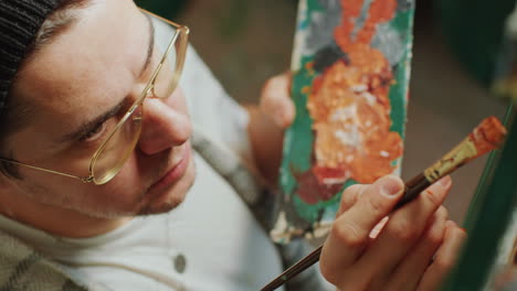 concentrated artist holding palette and painting with brush on canvas