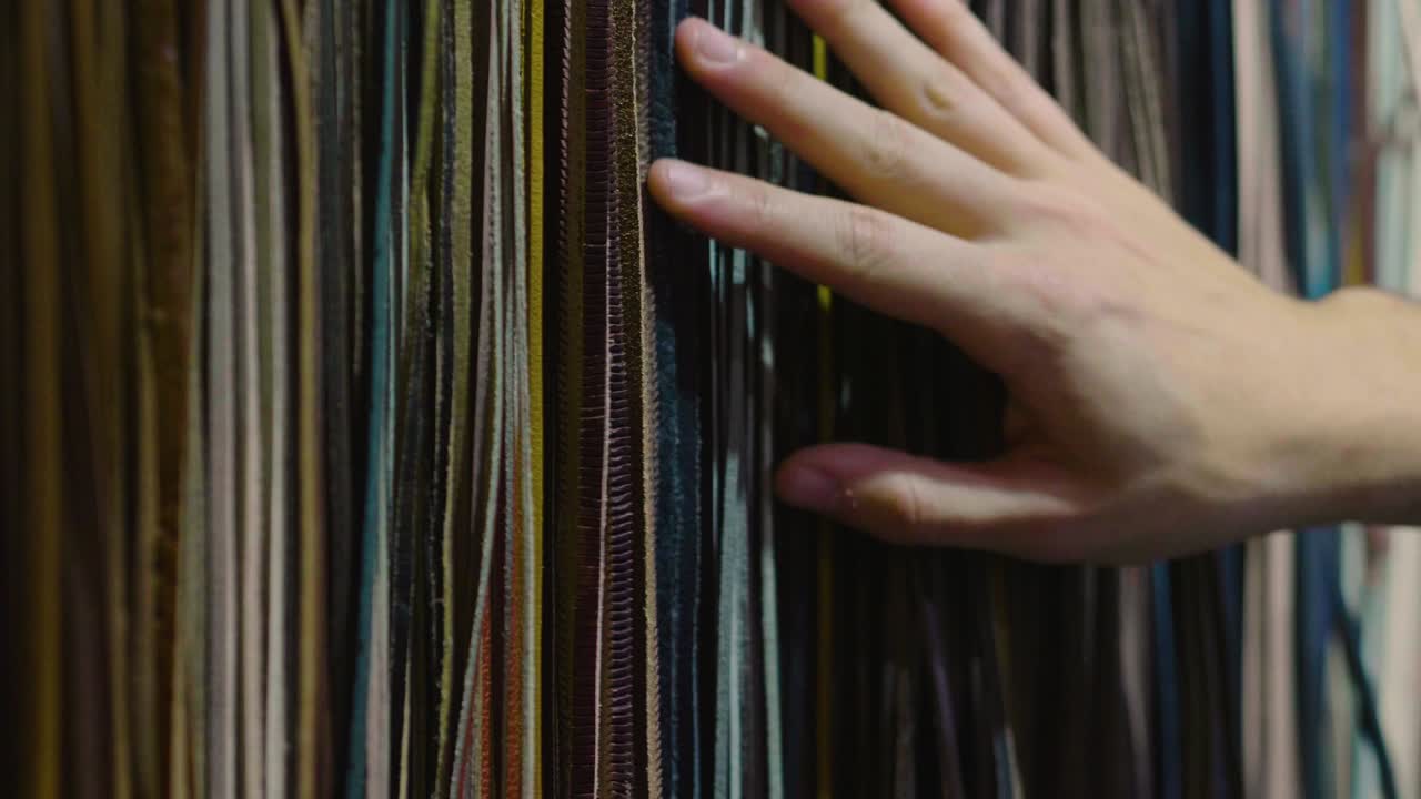 A mix of leather and leather belts in different colors and a hand that touches to test the quality of the material.