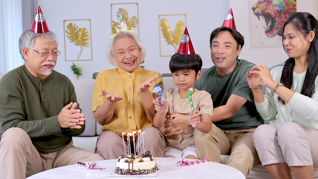 3世代が、ケーキやパーティー帽子、明るい室内照明で、楽しい誕生日のお祝いを楽しんでいます。