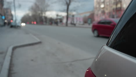 vista de cerca de un coche estacionado con un coche rojo que se acerca por detrás y otro coche con faros visibles en la distancia
