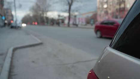 close-up view of a parked car with a red car approaching from behind and another car with headlights visible in the distance