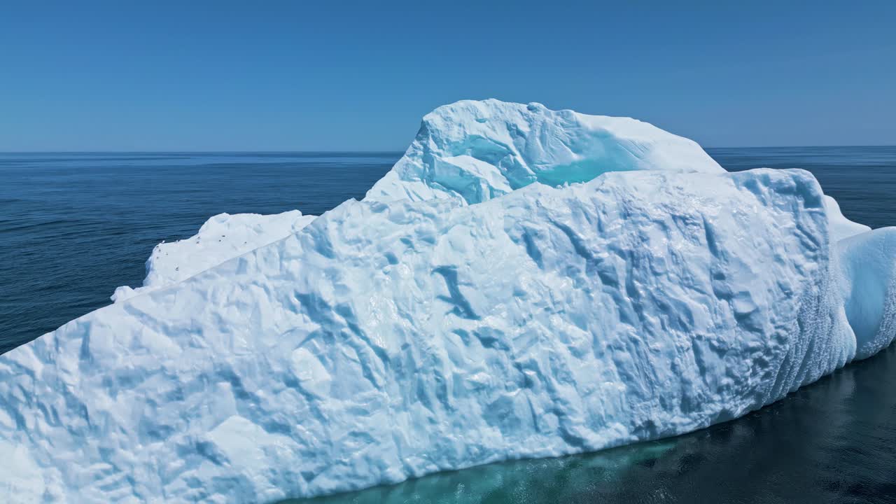 Aerial footage of a large iceberg off Flatrock, Newfoundland, featuring vivid turquoise meltwater in calm Atlantic waters.