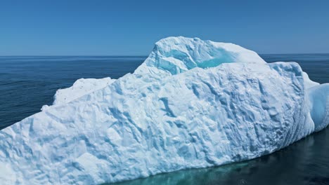 aerial footage of a large iceberg off flatrock, newfoundland, featuring vivid turquoise meltwater in calm atlantic waters.