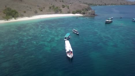 Indonesian-Tourist-ship-cruiser-off-the-coast-of-Pink-Beach-in-Komodo-Island,-Indonesia---Aerial-Ascend-fly-back-Reveal