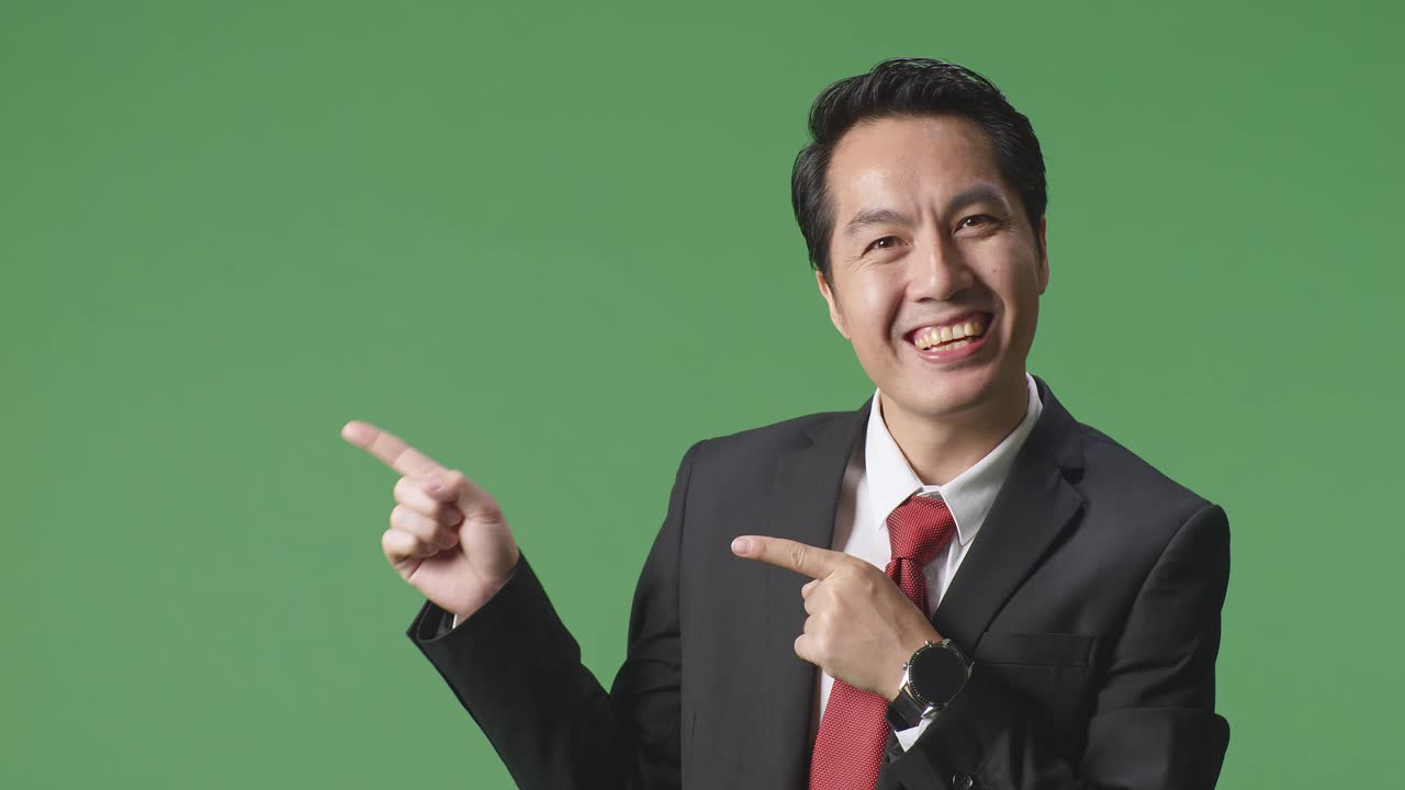 초록색 스크린에 서 있는 동안 을 가리키는 미소를 가진 아시아 사업가