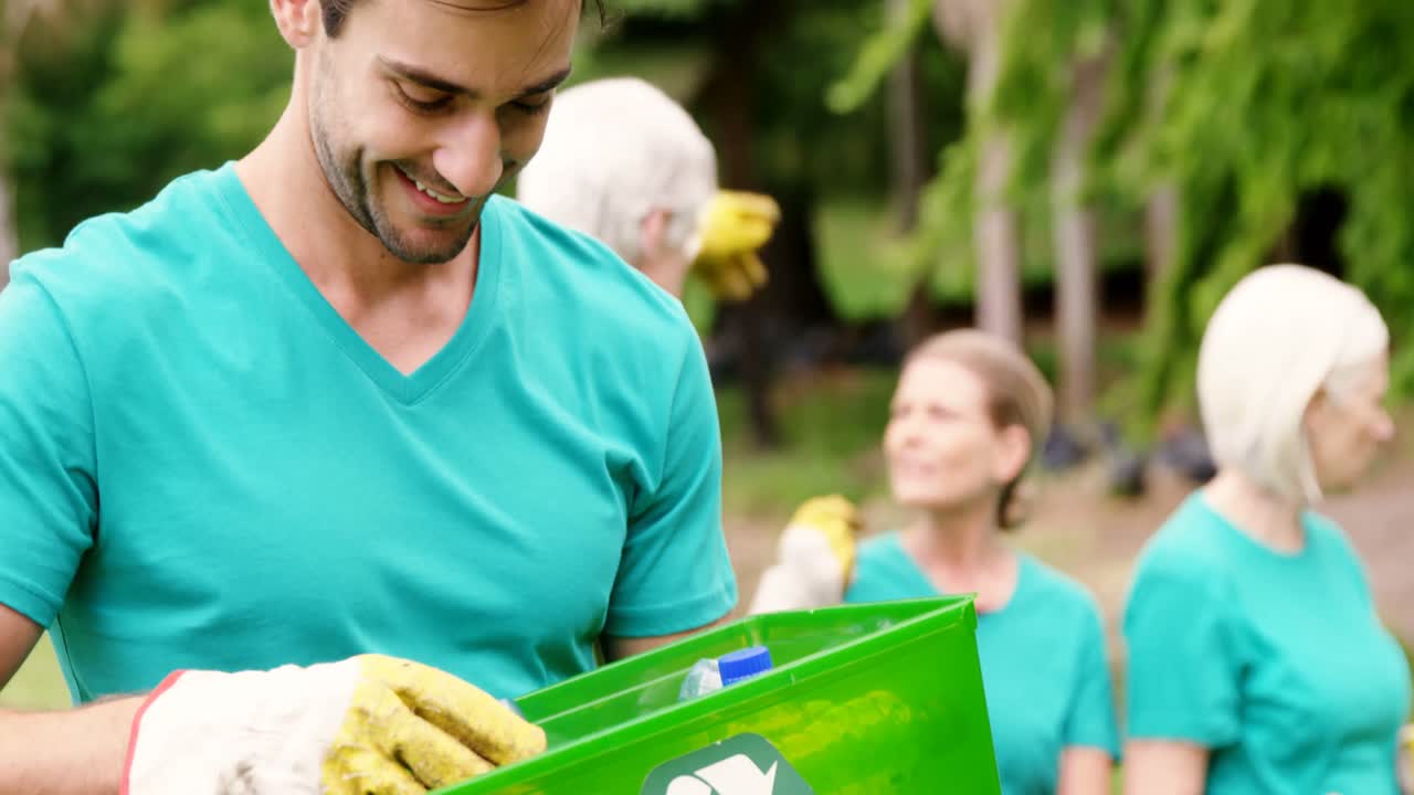 voluntario sosteniendo un contenedor de reciclaje en el parque