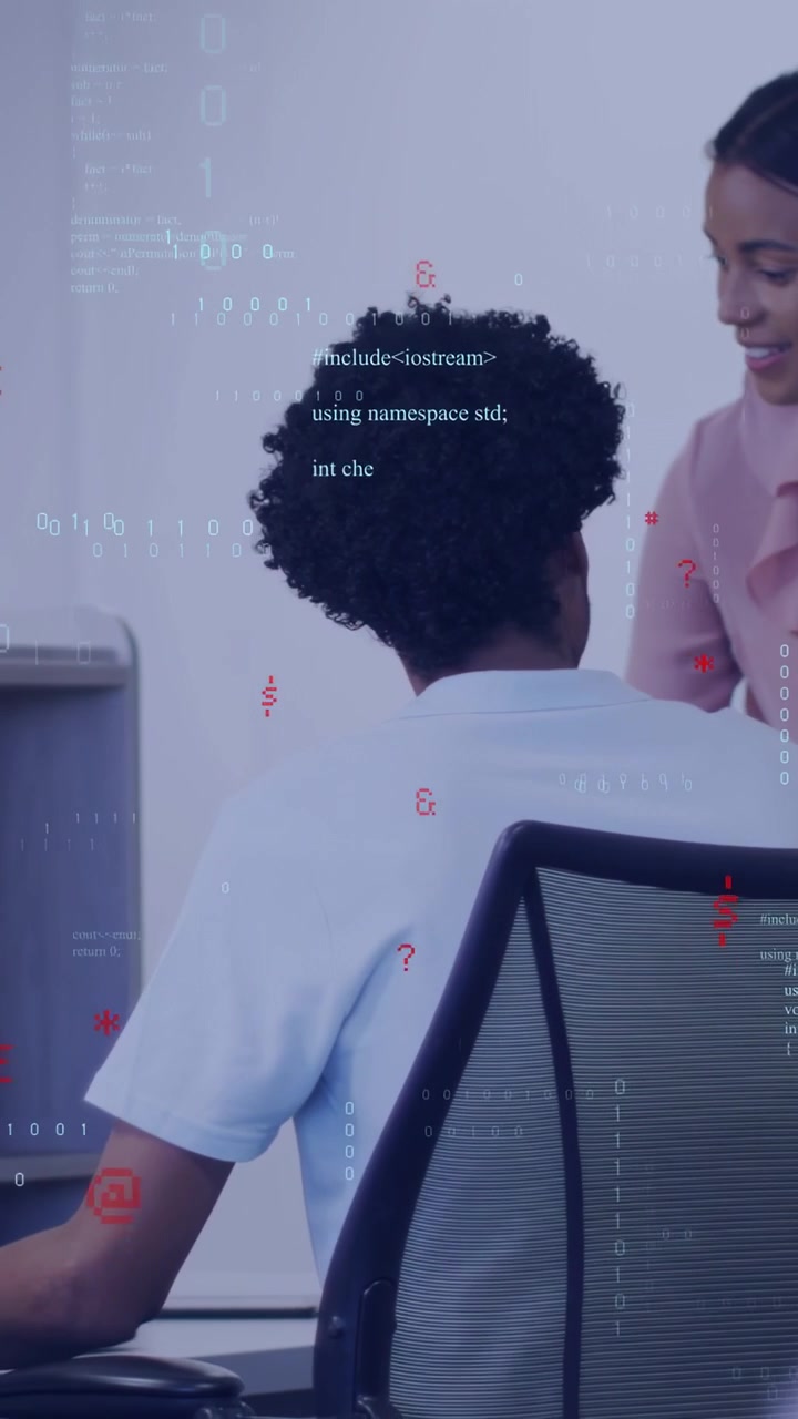 Vertikal video: Mand taster på bærbar computer, mens kvindelig leder nærmer sig, assisterer, teknisk kode vises.
