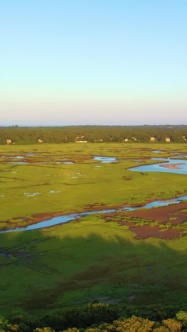 Ripresa aerea verticale con drone sui tortuosi canali delle paludi salmastre e sulle verdi zone umide, con una calda luce dorata. Paesaggio costiero con inquadratura alta, con riflessi di insenature serpeggianti e orizzonte a strati, b-roll cinematografico in 4K.