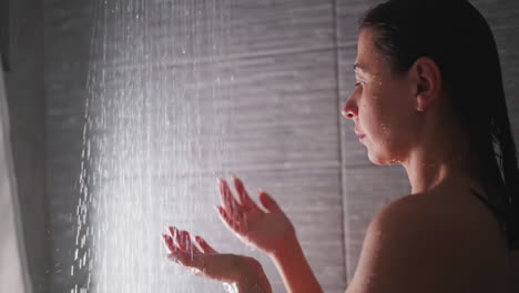 woman puts hands under shower sprays in bathroom. contemplative lady touches hot liquid flow by elegant palms in washroom. spa relaxation at home