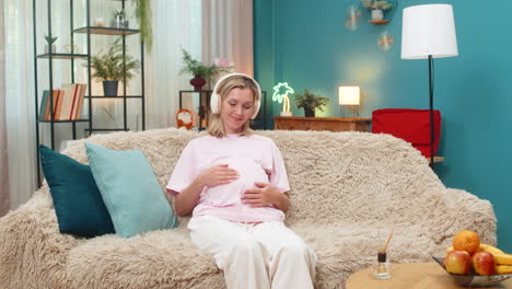 pregnant woman inhaling aroma from diffuser with headphones relaxing music hugging belly calm deep