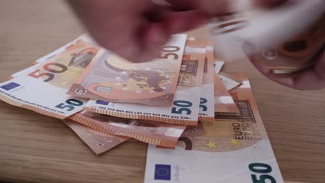 Primer-Plano-De-Un-Hombre-Contando-Un-Juego-De-Billetes-De-50-Euros-Y-Colocándolos-Sobre-La-Mesa