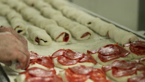 baker rolling dough with salami cuts in the bakery kitchen - salami bread rolls - close up
