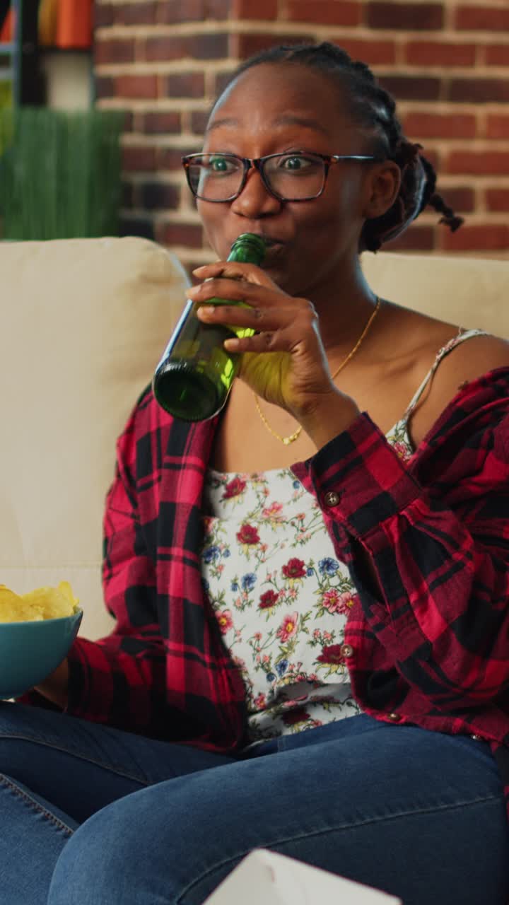 Vertical video: Smiling person holding bowl of snacks watching show
