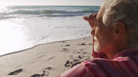 Senior-man-sitting-looking-away-at-the-beach