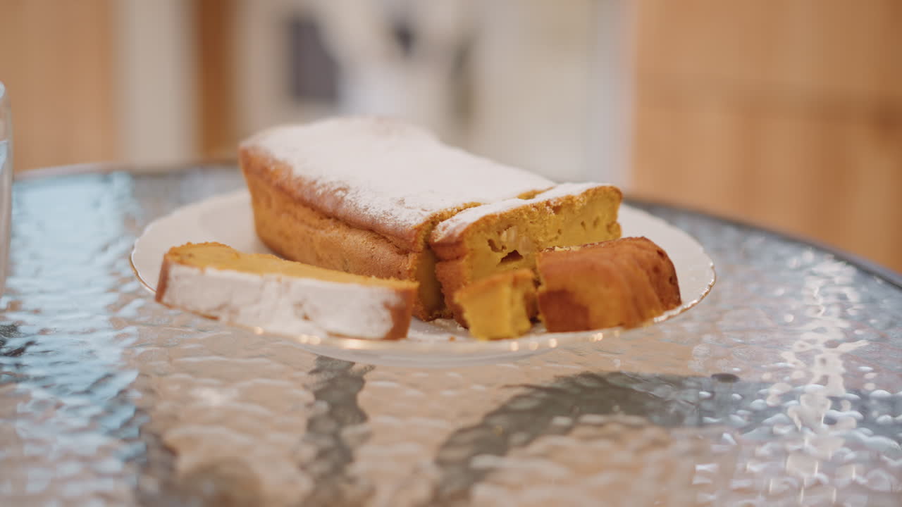 Pumpkin loaf on glass table coffee home baker arranging slice beside latte powdered sugar dusting warm midday kitchen light soft bokeh background golden crumb texture inviting cozy atmosphere close