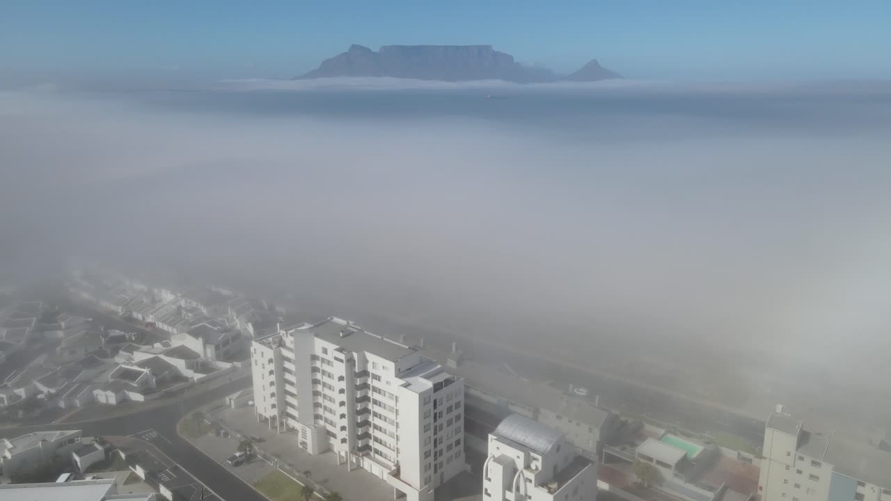 imágenes aéreas de bloques de apartamentos en el lado del océano con niebla espesa y montaña de mesa en el fondo lejano