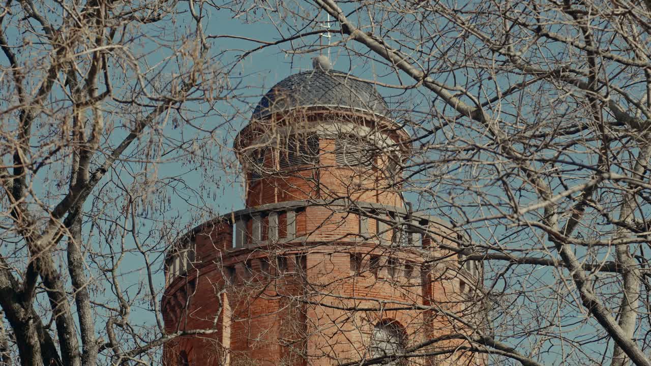 Historiskt tegeltorn med kupoltak sett genom nakna trädgrenar