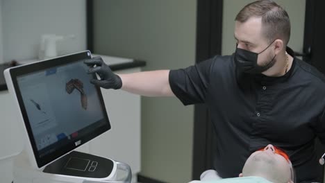 doctor scans the patient's teeth in the clinic. the dentist holds in his hand a manual 3d scanner for the jaw and mouth. dental health. creates a 3d model of teeth and gums on a medical monitor.