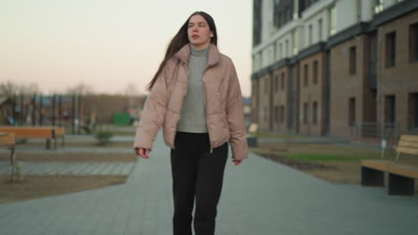 young girl in a peach jacket and black trousers is rollerblading along a paved path in a serene urban park. the scene captures the peaceful atmosphere with benches and people sitting in the background