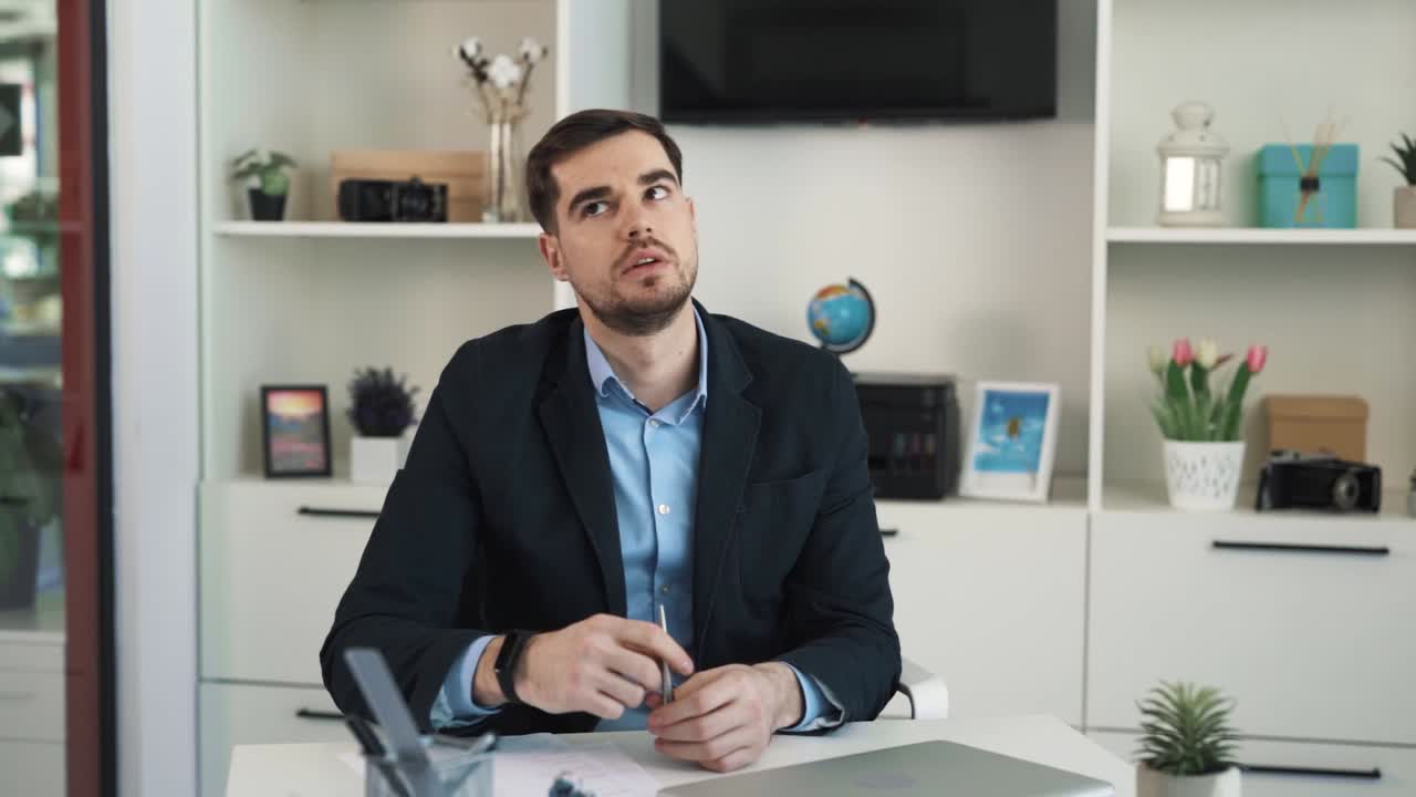 The young man is sitting at a desk in the office, he is saddened and frustrated, displaying his failure at work
