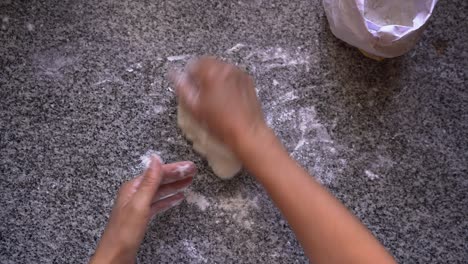 Female-chef-kneading-pastry-dough-on-floured-kitchen-surface,-overhead-closeup