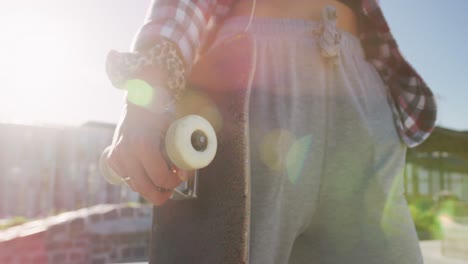 Midsection-of-caucasian-woman-holding-skateboard-on-sunny-day