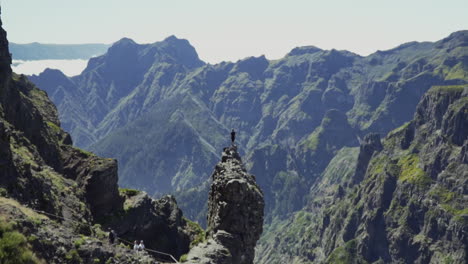 alejándose del hombre parado sobre una roca peligrosa para revelar una vasta cadena montañosa