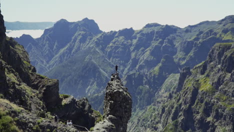 zooming out from man standing on perilous rock to reveal vast mountain range