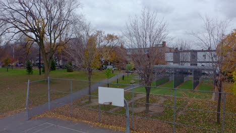 drone descending on a public park with a batting cage and a basketball court on a grey autumn day