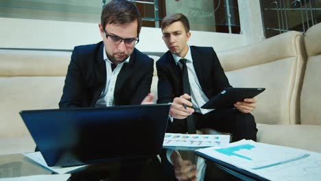 two businessmen work with documents and a laptop in the lobby of the hotel