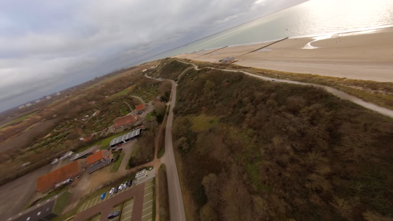 Drone flying fast towards and over a high sand dune at the beach, revealing the touristic town behind it