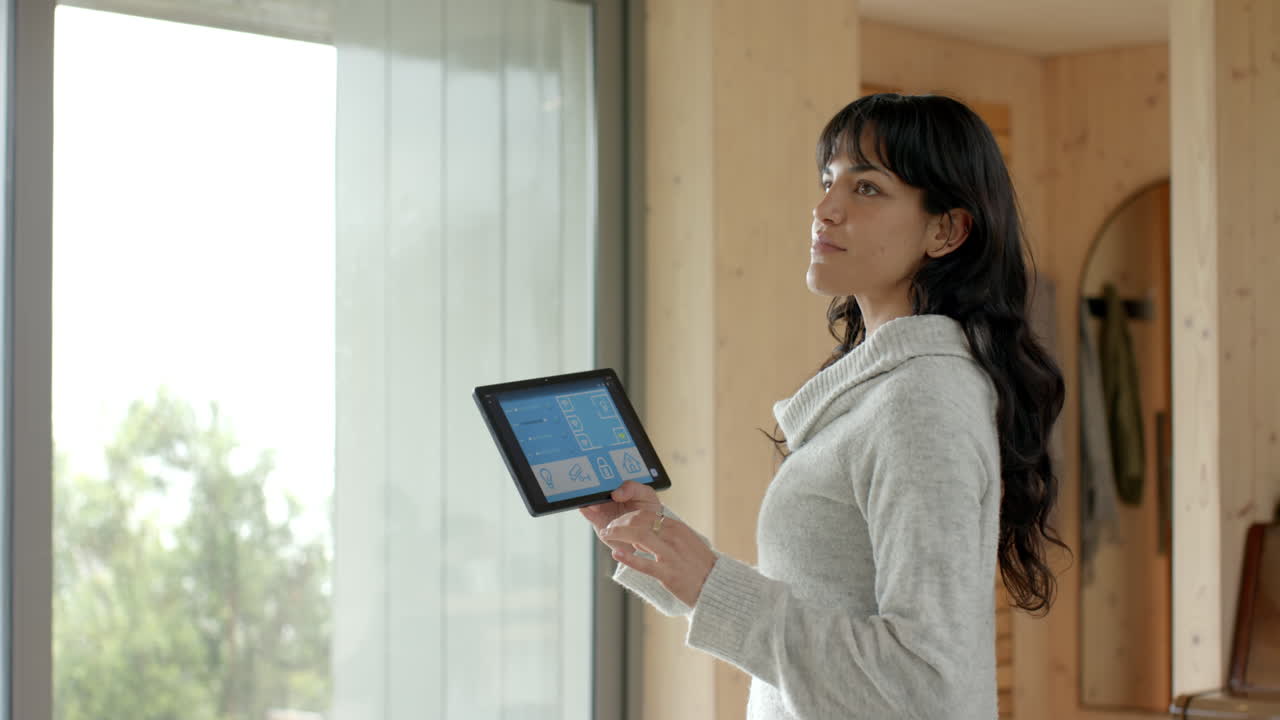 Smiling woman using tablet to control smart home technology by window, copy space