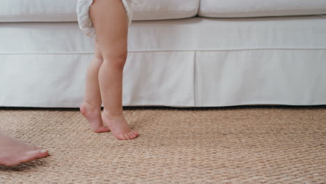 baby taking first steps toddler learning to walk with mother gently helping infant teaching child at home motherhood trust