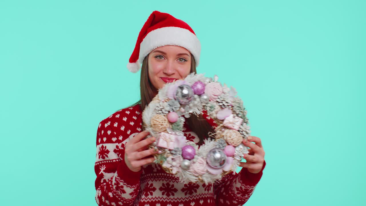 una chica adulta sonriente con un suéter de navidad rojo sostiene el dedo del punto de elevación en el juguete de la corona festiva