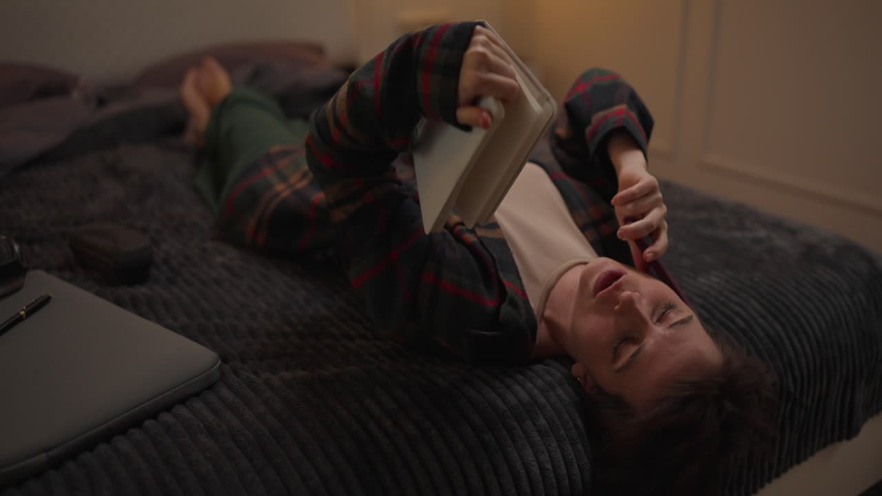 Woman talking on the phone while lying on bed with notebook and laptop